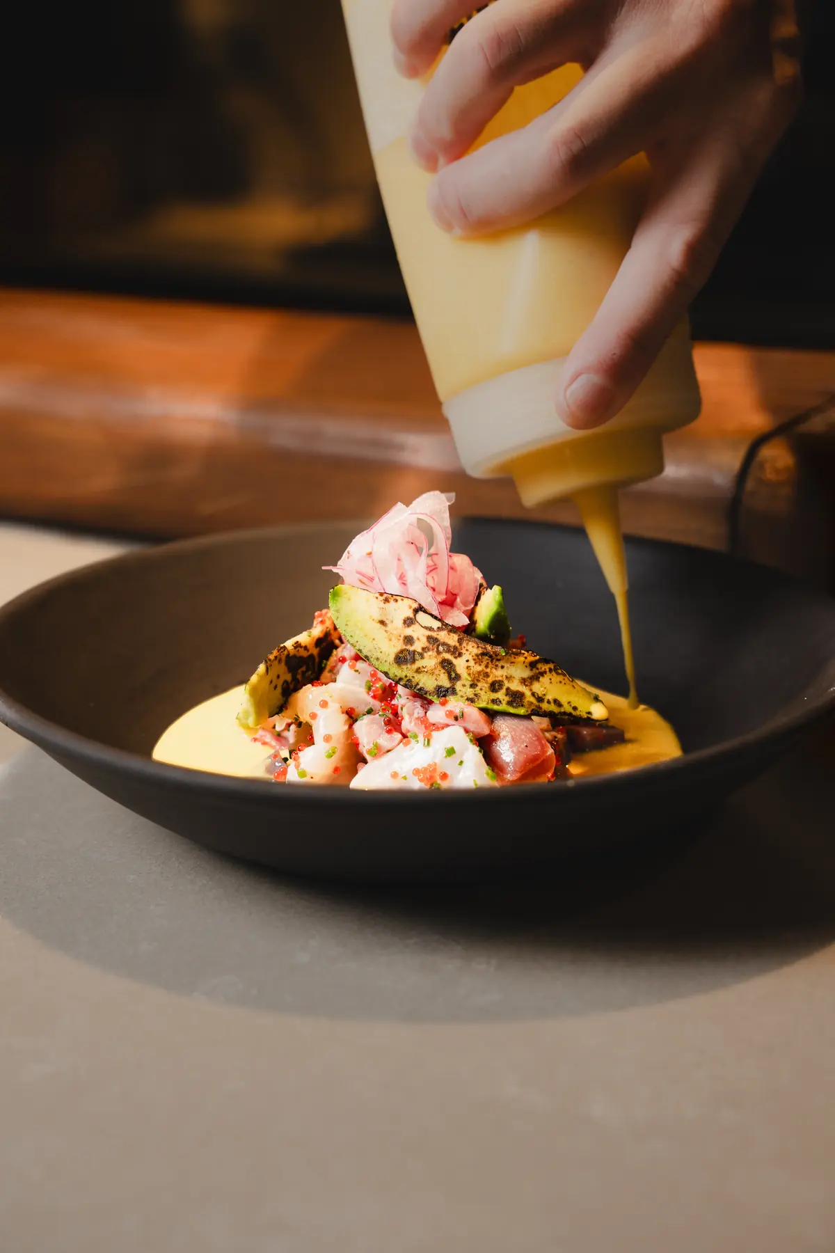 La leche de tigre cae sobre el ceviche, con aguacate a la llama y cebolla encurtida
