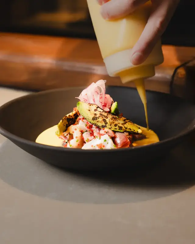 La leche de tigre cae sobre el ceviche, con aguacate a la llama