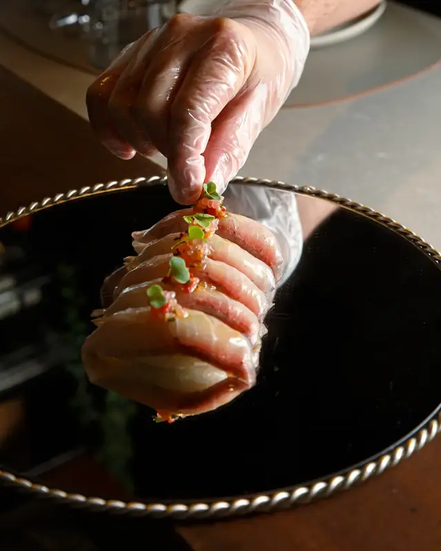 Una mano con guante termina los nigiris sobre el plato de espejo